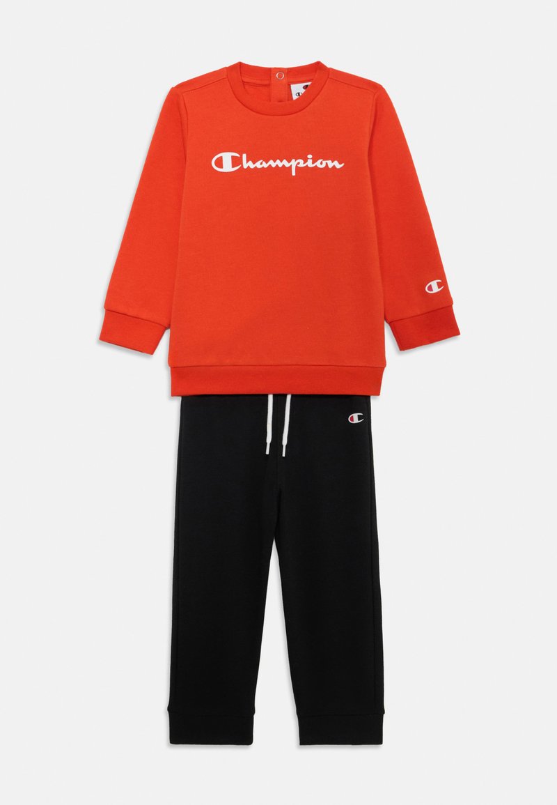 Sweatshirt vermelho com ologotipo "Champion" e calças de fato pretas com cordão. Ambos feitos de algodão suave, com punhos e faixa da cintura canelados.