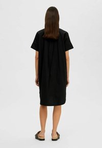 Svart klänning med kort ärm och lös passform, knälång längd och en detalj i sömmen bak. Bärs med platta sandaler. Slät tygstruktur.