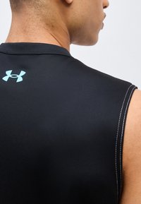 Κοντινό πλάνο ενός ατόμου που φοράει μαύρο αμάνικο αθλητικό τοπ με ανοιχτό γαλάζιο λογότυπο Under Armour στο πάνω μέρος της πλάτης.