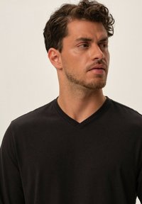 Czarna, długosleeve, koszulka z dekoltem w kształcie v zaprezentowana na męskim modelu, charakteryzująca się gładką fakturą i dopasowanym krojem, idealna na casualowy wygląd.