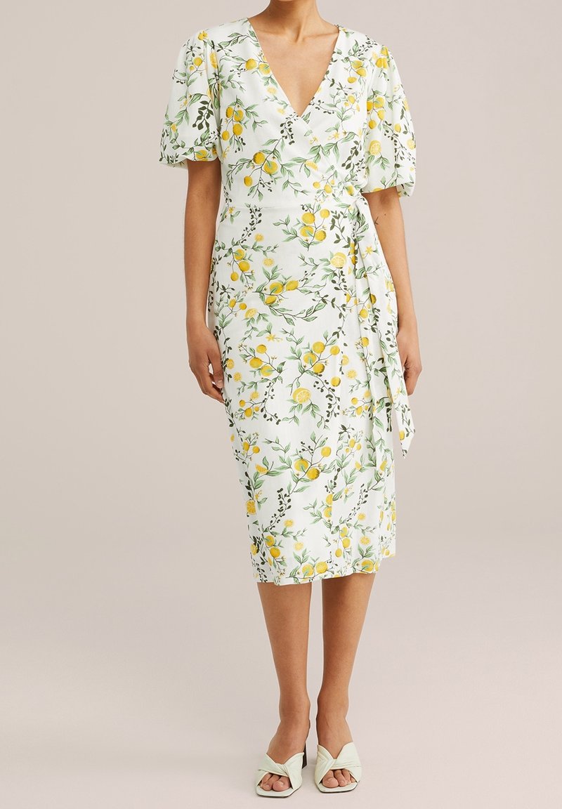 Blumenkleid mit Zitronen- und Grünpflanzenmuster, kurzen Puffärmeln, V-Ausschnitt und seitlichem Bindeband. Weißer Hintergrund mit grünen Akzenten.