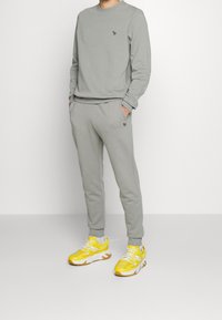 Sudadera gris y pantalones de chándal a juego, hechos de un material suave, con un logotipo bordado. Zapatillas deportivas amarillas brillantes con acentos blancos.