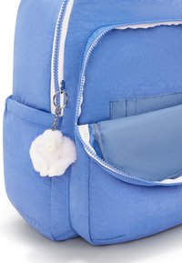 Blå ryggsäck med texturerat tyg, vita dragkedjor, sidoficka och en fluffig vit nyckelring som liknar ett litet djur.