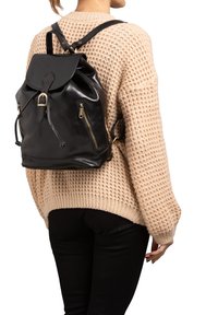 Zwarte leren rugzak met verstelbare banden, ritszakken en een omgevouwen klep. Gestructureerde afwerking met gouden hardware accenten.