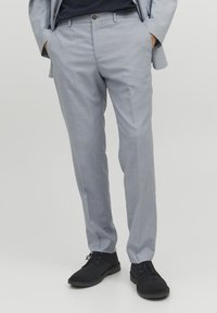 Lichtgrijze broeken van zacht materiaal, met een platte voorkant, slim fit en zijzakken. Gecombineerd met zwarte schoenen.