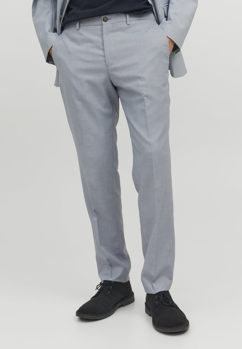 Lichtgrijze broeken van zacht materiaal, met een platte voorkant, slim fit en zijzakken. Gecombineerd met zwarte schoenen.