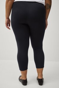 Navyblauwe leggings van rekbare stof, aansluitend ontwerp met een lengte tot halverwege de kuit, en een gladde textuur. Zwarte instap schoenen zichtbaar.