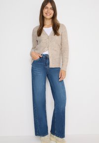 Beige neulecardigan, jossa on V-pääntie ja napit, yhdistettynä vaaleansinihin leveälahkeisiin farkkuihin. Kankaassa on teksturoitu pinta.