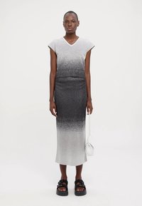 Rochie tricotată cu un gradient de la alb la negru, având o decolteu în V, mâneci scurte și o siluetă ajustată. Asortată cu sandale groase și o poșetă mică.