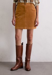 Tan corduroy minirok met knopen aan de voorkant en zakken, gecombineerd met kniehoge bruine leren laarzen, met een slank ontwerp en een soepele textuur.