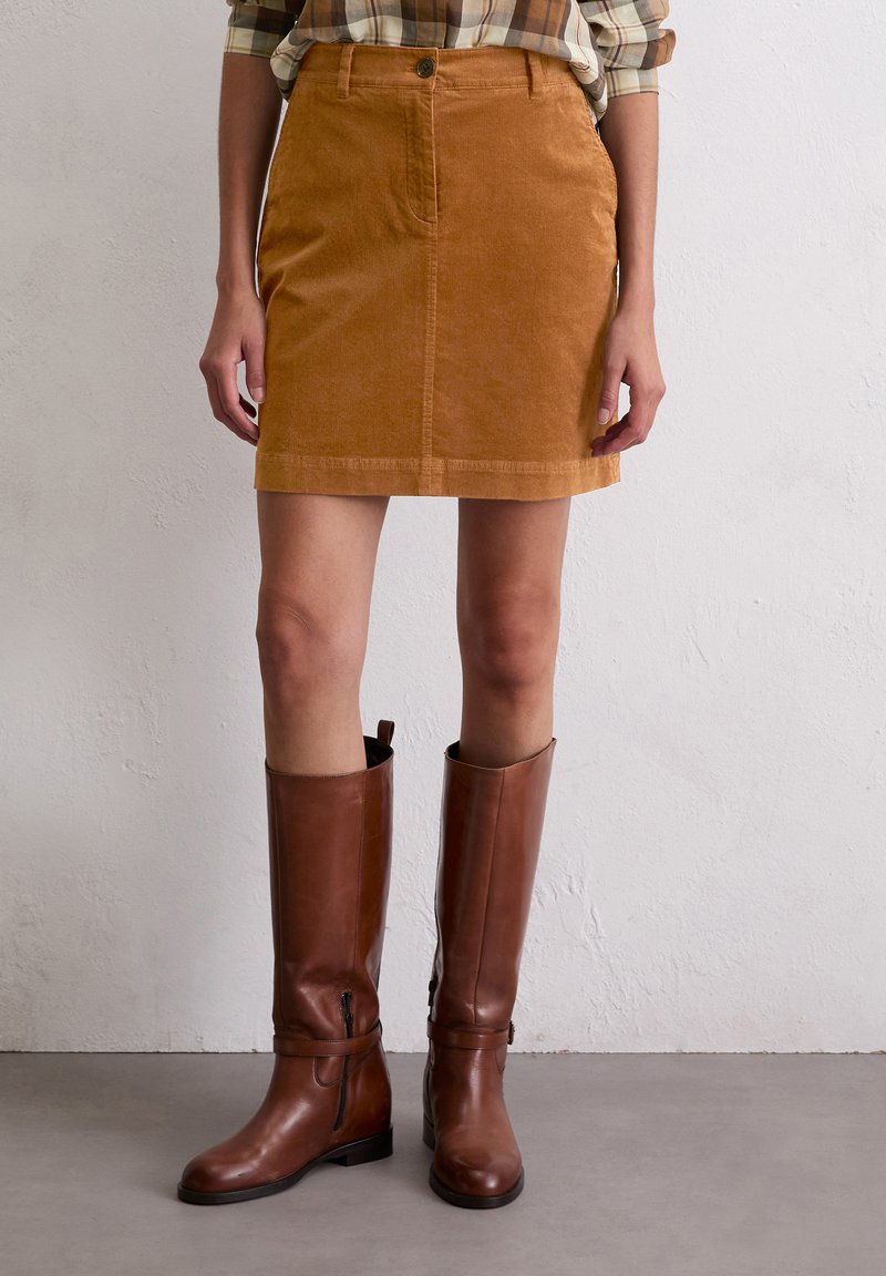 Tan corduroy minirok met knopen aan de voorkant en zakken, gecombineerd met kniehoge bruine leren laarzen, met een slank ontwerp en een soepele textuur.