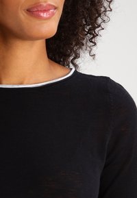 Schwarzer Pullover mit rundem Halsausschnitt und grauem Besatz, weichem Material und tailliertem Design, das dezente Rippungen an den Schultern zeigt.