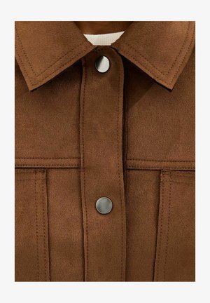 Chaqueta de ante marrón con dos botones de presión plateados, costuras visibles y cuello ancho sobre una camisa blanca.