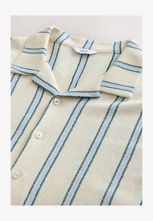 Chemise à manches courtes rayée avec une base beige, présentant des rayures verticales bleu sarcelle et bleu clair. Tissu texturé et fermetures à boutons blancs.