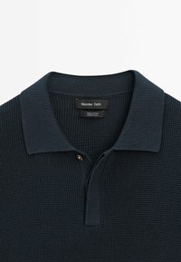 Polo en maille texturée bleu marine foncé avec col et un bouton, avec une étiquette Massimo Dutti à l'intérieur de l'encolure.