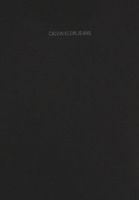 T-shirt en coton noir avec col rond et manches courtes. Logo "CALVIN KLEIN JEANS" imprimé en gris contrastant au-dessus du centre.