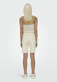 Pantalones cortos de mezclilla de color beige claro con un corte holgado, con un dobladillo deshilachado, combinados con un top corto de punto texturizado en crema con ribetes negros.