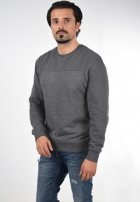 Grå sweatshirt med teksturert panel, lange ermer, rund hals, ribbede mansjetter og hem. Båret med blå skrukkete jeans.