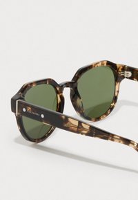 Óculos de sol redondos em padrão tartaruga com lentes verdes e logótipo "AllSaints" na haste contra um fundo branco.