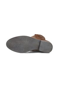 Bruine suède boot die op zijn zij ligt en een versleten rubberen zool met textuur en hak toont op een witte achtergrond.