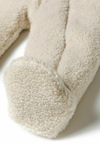 Närbild av ett mjukt, beige, fluffigt tyg som liknar shearling, med fokus på en rundad, texturerad manschett eller ärmslut.
