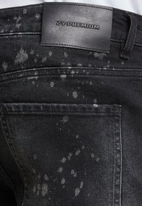 Czarne dżinsy z wyszłym na światło szarym splaterowaniem, z teksturowaną czarną skórzaną metką z napisem "ZY PREMIUM" w talii.