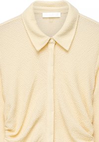 Kreemivärvi tekstuuriga kangast särk klassikalise kraega ja ühe nähtava nööbiga kaelusel.