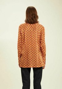 Chemise à manches longues présentant un motif floral multicolore sur fond jaune, avec une coupe décontractée et des poignets à boutons.