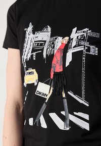 Musthave mustrõngastega must T-särk, millel on graafiline disain naisest punases kleidis, kõrgete kontsade ja kotiga, koos linna siluettide ja taksode illustratsioonidega.