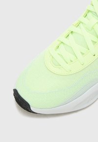 Chaussure de sport néon vert clair avec un dessus en maille texturée, des lacets plats, et une semelle en caoutchouc noire. Accent de semelle intermédiaire lisse blanche.