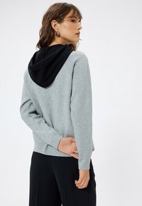 Grå sweatshirt med sort hætte, der har lange ærmer og et tætsiddende slids. Blød tekstur og afslappet design, der er velegnet til hverdagsbrug.