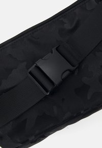Svart kamuflasjepose med teksturert stoff, med en glatt glidelås og holdbar spenne med svart plastrem.