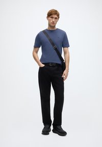 Ανοιχτό μπλε T-shirt με στρογγυλή λαιμόκοψη, άνετη εφαρμογή. Μαύρο παντελόνι με ίσια γραμμή. Μαύρα αθλητικά παπούτσια με υφή. Ρυθμιζόμενο μαύρο λουρί που διαπερνά το σώμα.