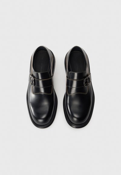 Une paire de chaussures à boucle en cuir noir poli avec des bouts ronds et des boucles en argent, vue du dessus sur un fond blanc.