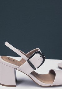 Blush pink højhælede sandaler med en bred rem og en spændeaccent, der har en chunky hæl og en glat, mat overflade.