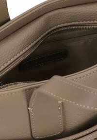 Intérieur d'un sac à main en cuir beige avec une surface texturée, fermeture éclair et détails de couture légers. Étiquette de marque visible à l'intérieur.