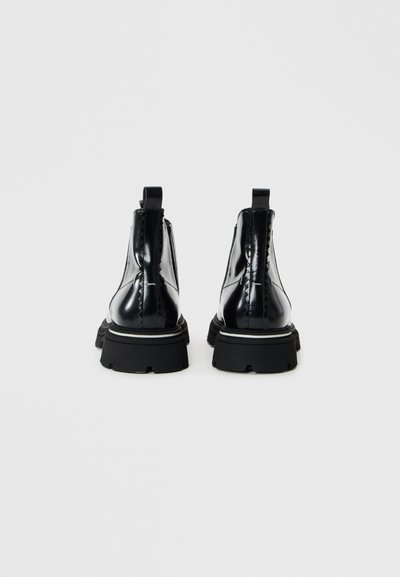 Botine din piele lacuită neagră, cu talpă din cauciuc, cu bandă de tragere și detalii de coasere dublă. Prezintă un design voluminos și un finisaj texturat.