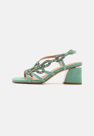 Green suede block heel sandal with jeweled chain-link straps and adjustable ankle buckle.