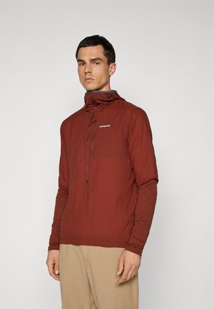 Red lightweight pullover jacket with a high collar, half-zip front, and long sleeves. Logo on the chest, smooth texture, and relaxed fit.