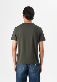 Olivengrønn t-skjorte med korte ermer og rund hals, laget av lett bomull, kombinert med blå denimjeans med klassisk fem-lommers design.