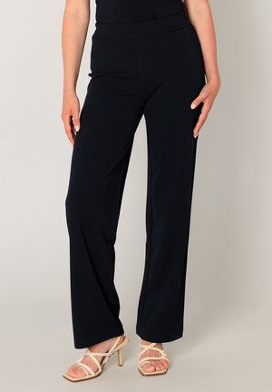 Marineblauwe wijde pijpen broek met een soepele textuur en een elastische tailleband, gecombineerd met lichte, met bandjes versierde hakken.