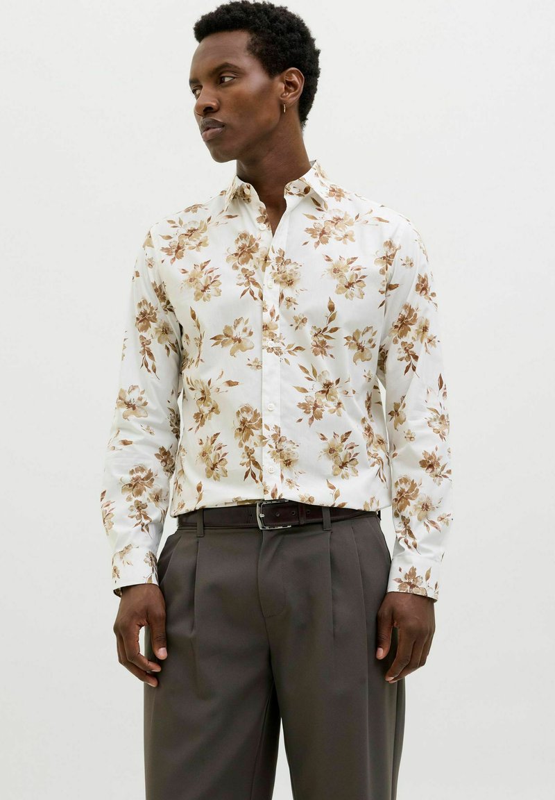 Bloemige button-up shirt met een witte achtergrond en bruine en beige bloemen; gecombineerd met grijze geplooide broeken.
