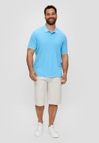 Lichtblauwe polo met korte mouwen en een kraag, gedragen met beige shorts en witte sneakers. Glad stoffen textuur, ontspannen pasvorm.