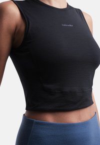 Musta urheilullinen crop-top, joka on valmistettu kosteutta siirtävästä kankaasta. Mallissa on istuva muotoilu, pyöreä pääntie ja violetti logo-yksityiskohta.