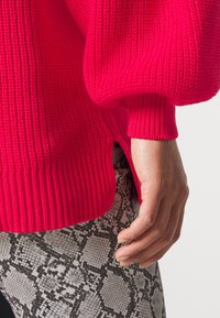 Lyserød strikket sweater med ribbede manchetter og kant, med sideslids. Kombination med sort/hvid slange mønster stof.