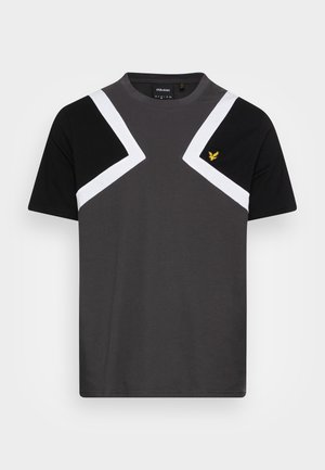 T-shirt pour homme en gris foncé, avec des manches noires et un motif zigzag blanc sur la poitrine. Petit logo jaune sur la gauche. Matériau doux.