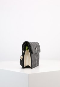 Černá kabelka s texturou hadího vzoru, s přehnutým klopovým víkem, stříbrným zapínáním a světle zbarveným interiérem. Kompaktní obdélníkový tvar.