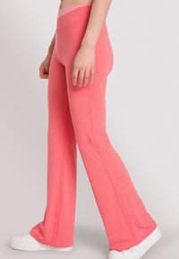 Roze flared yogabroek in een rekbare stof, met een hoge tailleband en een zachte textuur. Te combineren met witte sneakers voor een casual look.