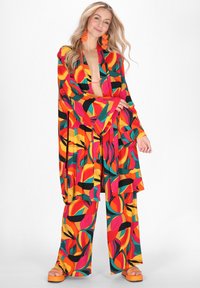 Jasny, dwuczęściowy zestaw składający się z luźnej bluzki w stylu kimono oraz szerokich spodni z abstrakcyjnym wzorem w kolorach czerwonym, żółtym, czarnym i zielonym.