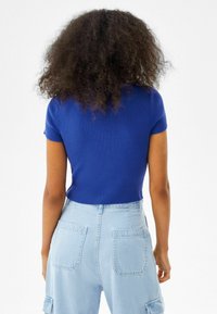 Königsblaues, geripptes T-Shirt mit kurzen Ärmeln, kombiniert mit hellblauen, hochgeschnittenen Cargo-Hosen mit aufgenähten Taschen und lockerer Passform.